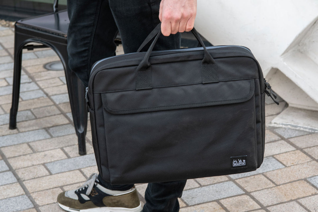 Brompton Metro City Bag M to torba w stylu teczki idealna na podróże służbowe, wykonana z wytrzymałego nylonu balistycznego 1680D z recyklingu z powłoką PU. Ma wymiary około 40 x 30 x 10 cm i pojemność 12 litrów, zapewniając dużo miejsca na zorganizowanie niezbędnych rzeczy do pracy.