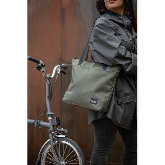Kobieta stojąca obok roweru z torbą materiałową Brompton Borough Tote - oliwkową.
