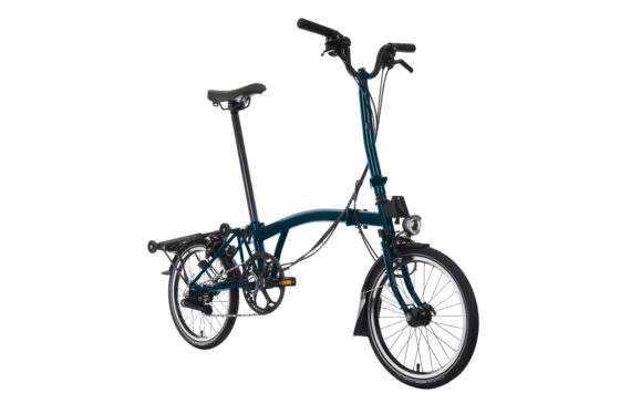 Turkusowy rower składany Brompton C-line M6R Ocean Blue z małą ramą i czarnymi oponami, ustawiony pionowo na białym tle.
