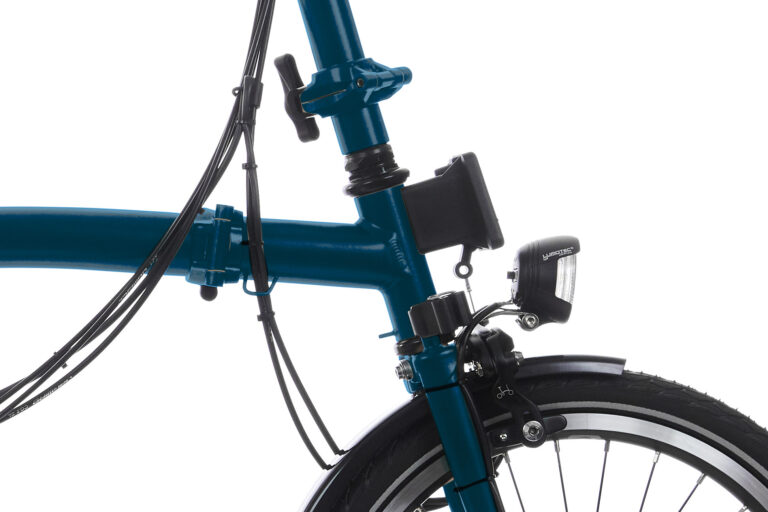 Zbliżenie przedniej części roweru Brompton C-line M6R Ocean Blue, przedstawiające widelec, reflektor i część koła na białym tle.