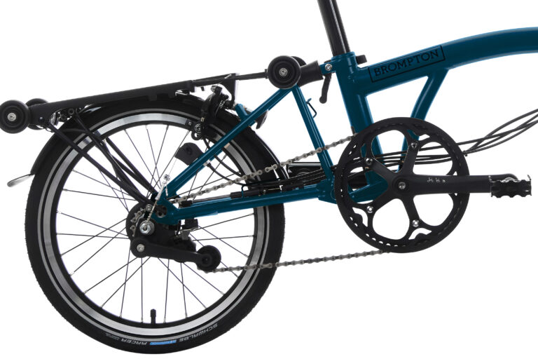 Zbliżenie na składany rower Brompton C-line M6R Ocean Blue, przedstawiające szczegóły tylnego koła, ramy i mechanizmu pedałów, odizolowane na białym tle.