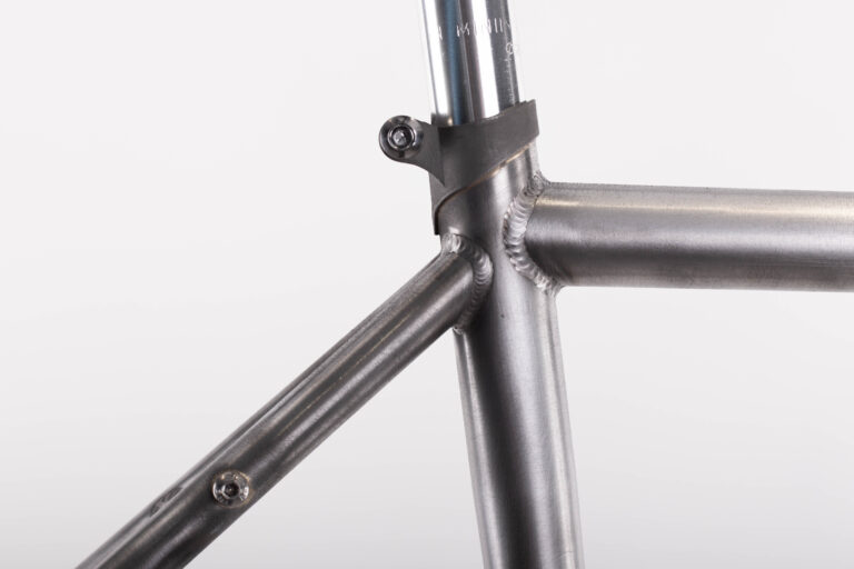 Zbliżenie spawanego złącza ramy roweru przedstawiające rurę podsiodłową, górną rurę i wsporniki siodełka z założonym zaciskiem siodełka.