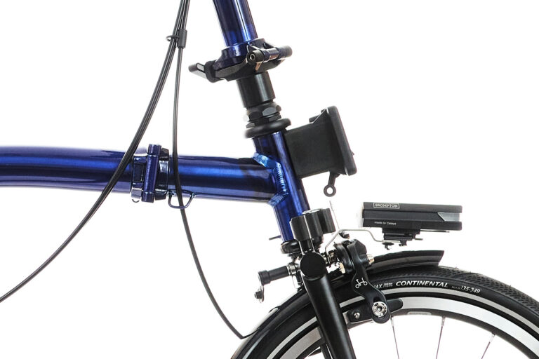 Zbliżenie przedniej ramy i widelca niebieskiego roweru, przedstawiające zamontowany czarny uchwyt na smartfon i elementy hamulca.