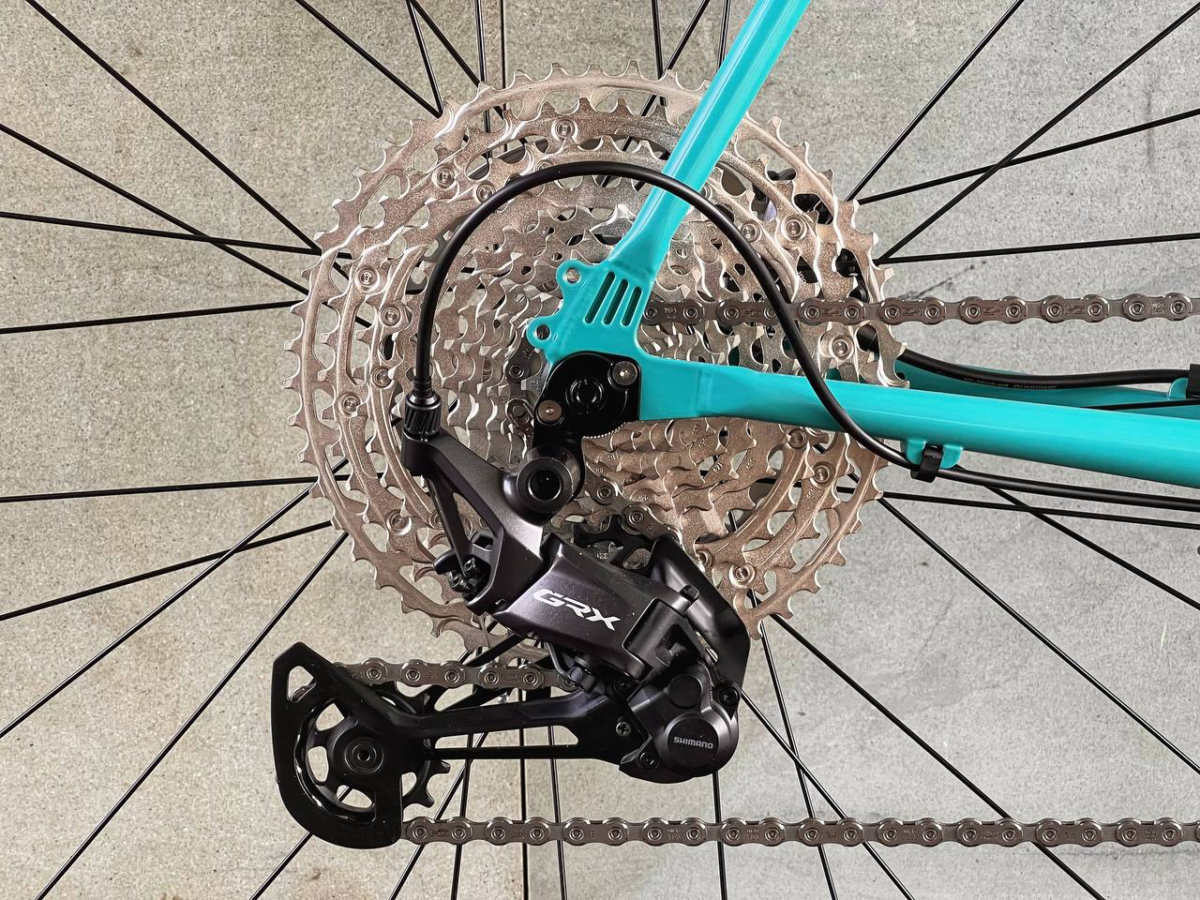 Zbliżenie tylnego koła roweru Antymateria Gravel Rock Shox w kolorze błękitnym, ukazujące przerzutkę Shimano GRX, dużą kasetę, łańcuch i smukłą ramę o szerokości 57 cm.