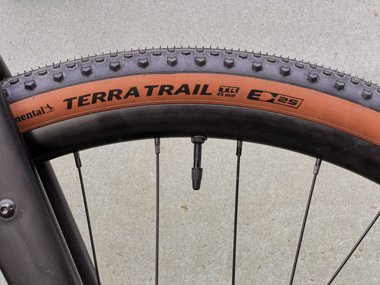 Zbliżenie opony „Terra Trail TR 45 mm” z widocznym wentylem na gładkiej nawierzchni — idealnej do przygód na oponie Anty Gravel CRE M - GRX400/600 - Czarny mat firmy Antymateria.