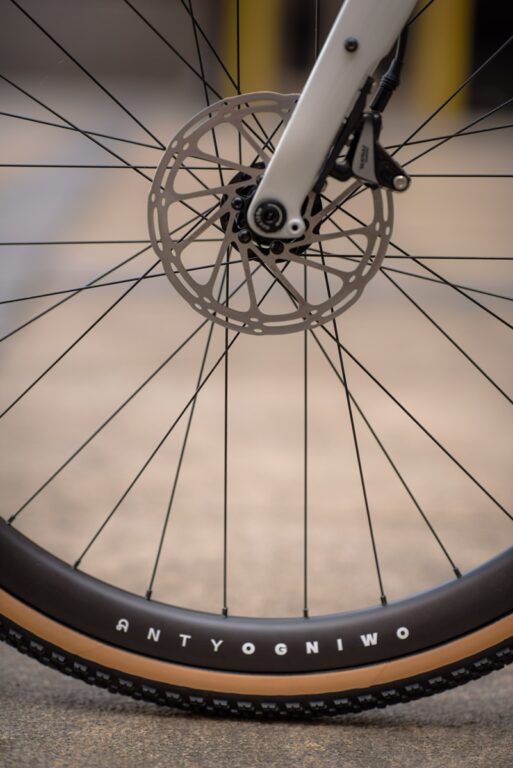 Zbliżenie koła rowerowego ze szczegółowym widokiem szprych, hamulca tarczowego i opony z napisem „antyogniwo.
