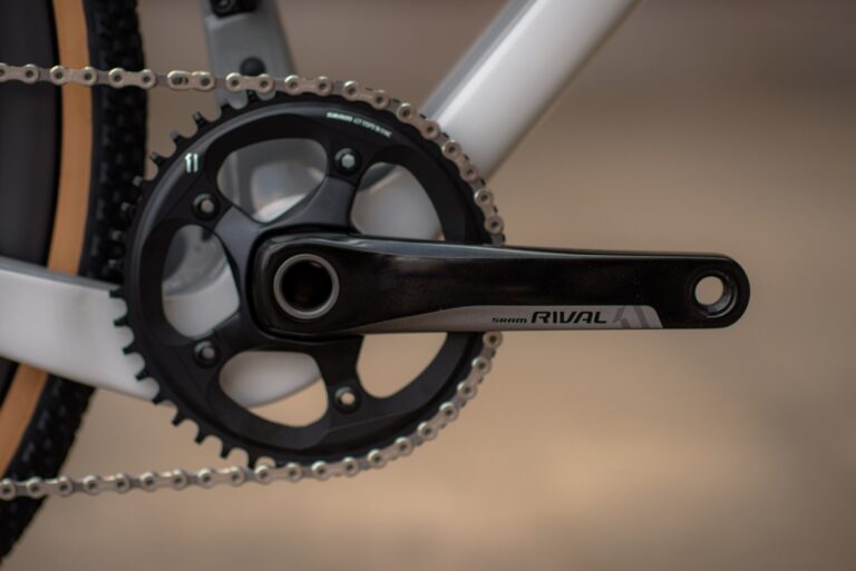 Zbliżenie na czarny mechanizm korbowy i łańcuch do konkurencyjnego roweru Sram na rowerze z białą ramą, ilustrujące elementy nowoczesnego roweru szosowego.