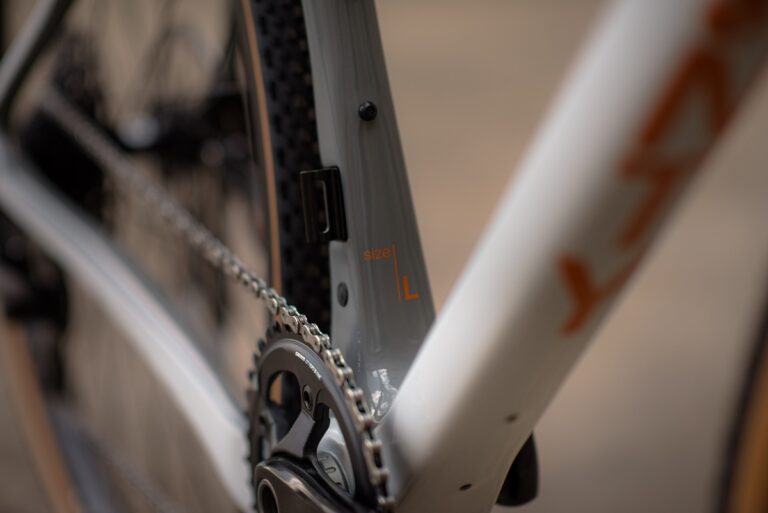 Zbliżenie na łańcuch rowerowy i przerzutki na ramie roweru z etykietą „rozmiar L”, skupiając się na szczegółach mechanicznych.