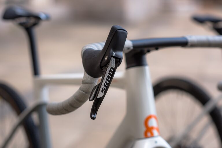 Zbliżenie na kierownicę roweru, przedstawiające szczegółową teksturę chwytu i dźwigni zmiany biegów, z lekko rozmytą ramą w tle.