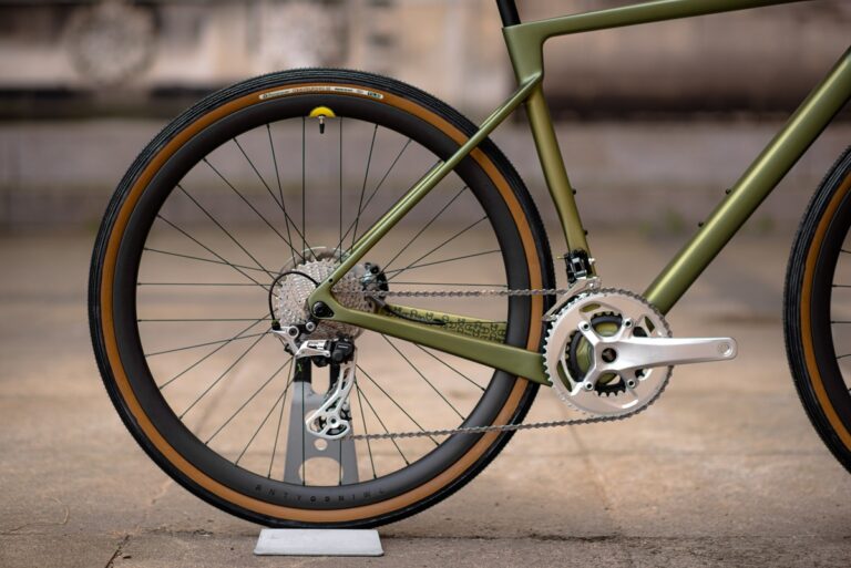 Zbliżenie na tylne koło i mechanizm przekładni zielonego roweru, ze szczególnym uwzględnieniem łańcucha i zębatek.