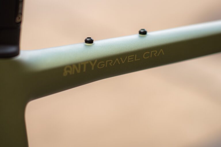 Zbliżenie na zieloną ramę roweru z wydrukowanym tekstem „antygravel.ca”, skupiające się na eleganckim wyglądzie i szczegółach.