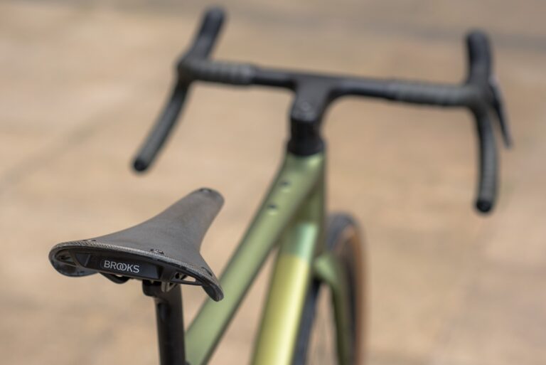 Zbliżenie roweru skupiające się na siodełku i kierownicy, z rozmytym tłem podkreślającym zieloną ramę roweru.