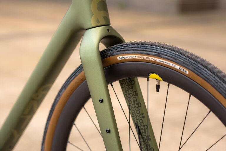 Zbliżenie na widelec rowerowy i oponę, podkreślając zieloną ramę i oponę szutrową panaracera.