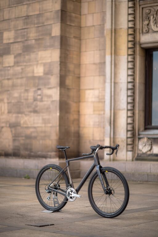 Czarny rower szosowy stoi na brukowanej uliczce obok dużego kamiennego budynku z ozdobnymi rzeźbami.