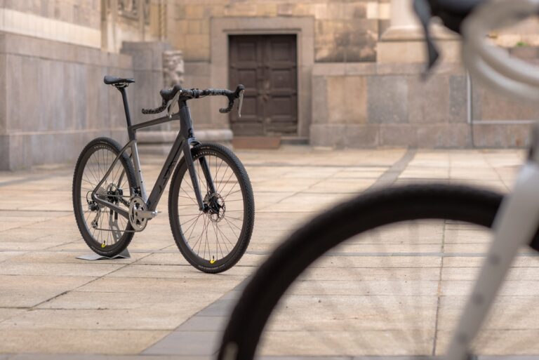 Czarny rower szosowy opiera się o kamienną ścianę obok zabytkowego budynku, na pierwszym planie widać koło innego roweru.