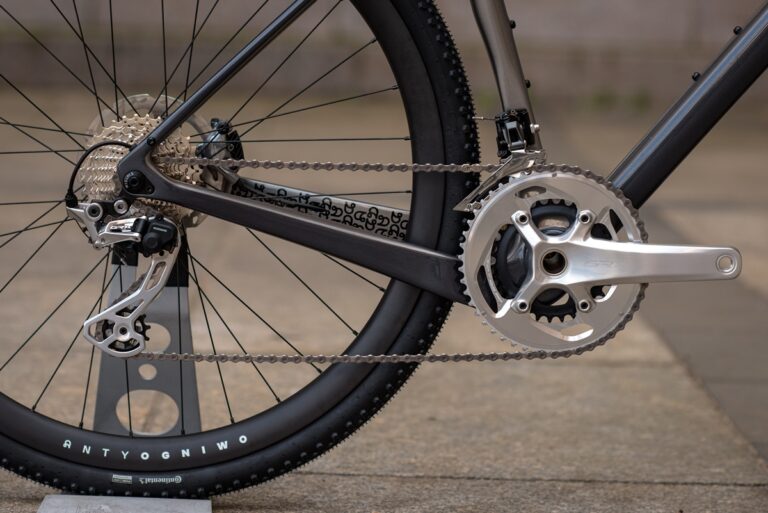 Zbliżenie na tylne koło, łańcuch i przekładnię nowoczesnego roweru, z uwydatnieniem przerzutki i mechanizmu korbowego.