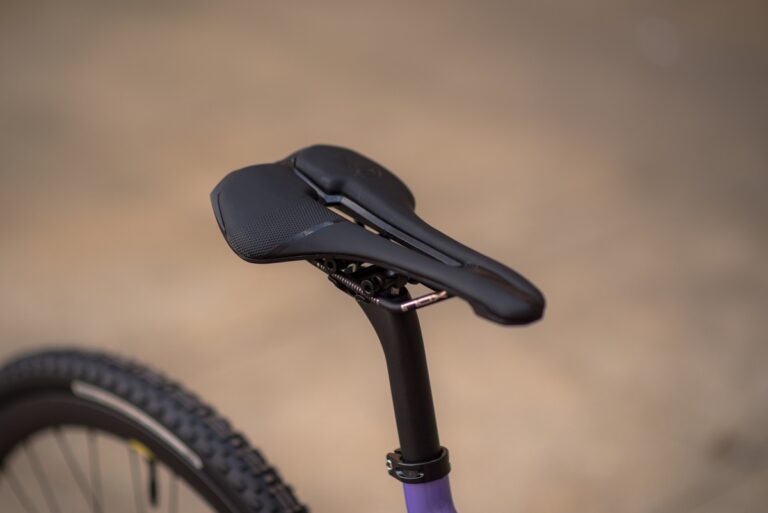 Zbliżenie na siodełko rowerowe Anty Gravel CRE XS (49 cm) - GRX 800 zamontowane na fioletowej sztycy, z rozmytym tłem podkreślającym fakturę siodełka.