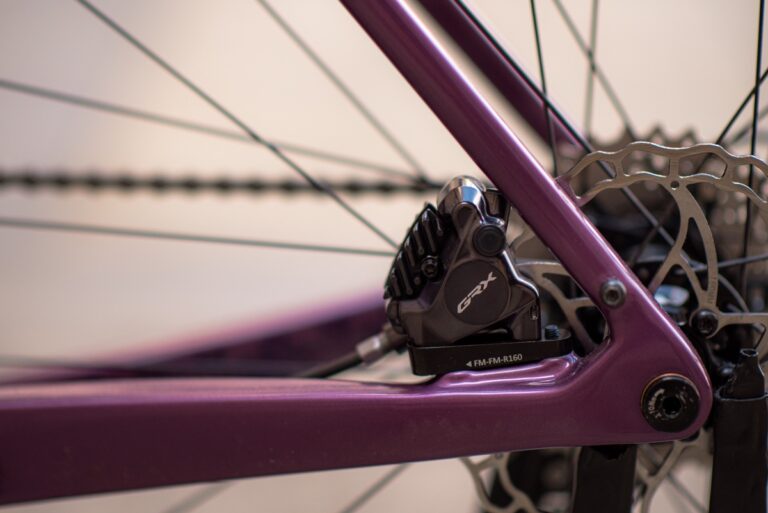 Zbliżenie na ramę roweru Anty Gravel CRE XS (49 cm) - GRX 800 przedstawiające tylny hamulec tarczowy i układ przerzutki, ze szczególnym uwzględnieniem klocka hamulcowego i szprych koła.