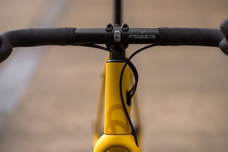 Zbliżenie na główkę ramy i kierownicę żółtego roweru, ze szczególnym uwzględnieniem eleganckiego projektu Anty Gravel CRE M (54 cm) i logo marki.