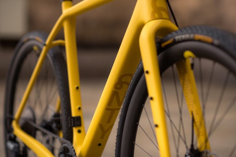 Zbliżenie na żółty rower Anty Gravel CRE M (54 cm) ze skupieniem na ramie i przednim kole, z widoczną na ramie marką.