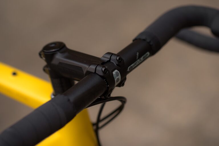 Zbliżenie na kierownicę i wspornik roweru Anty Gravel CRE M (54 cm), przedstawiające dźwignię hamulca i część żółtej ramy.