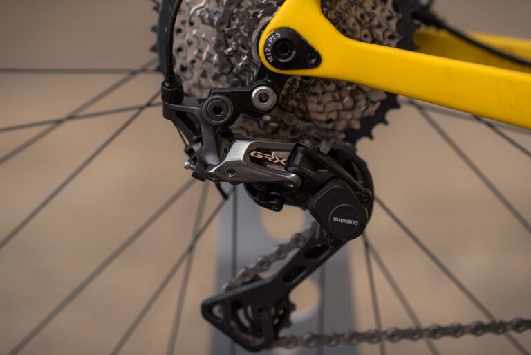 Zbliżenie na tylną przerzutkę rowerową Shimano GRX na żółtej ramie, ze szczególnym uwzględnieniem mechanizmu i przerzutek roweru szutrowego Anty Gravel CRE M (54 cm) - GRX 800.