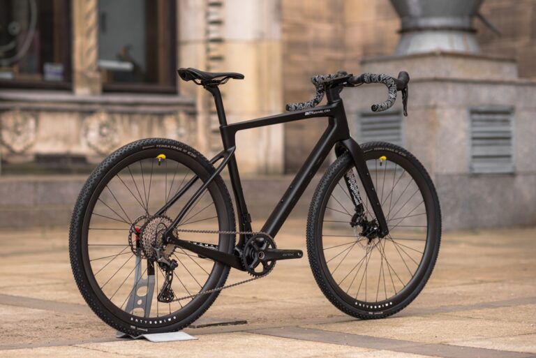 Nowoczesny czarny rower szosowy o aerodynamicznym kształcie, zaparkowany na tle zabytkowego budynku.