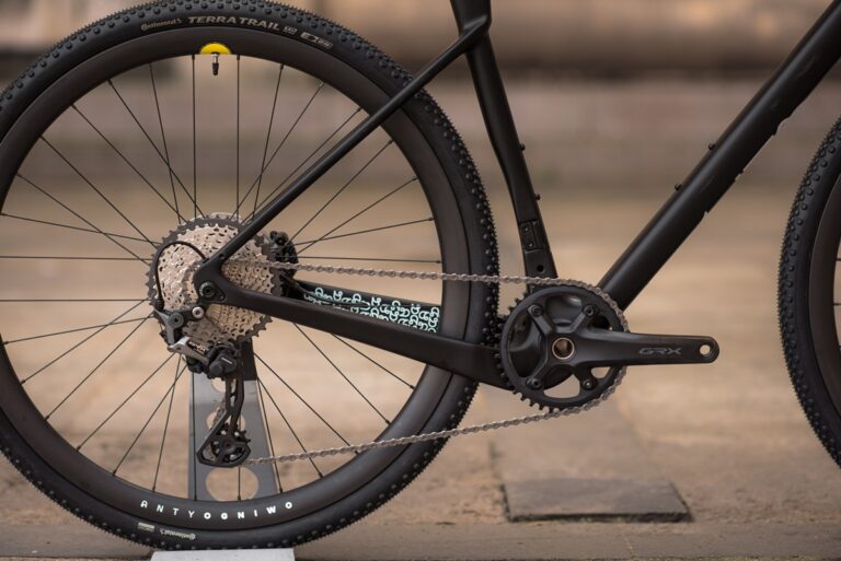 Zbliżenie na tylne koło, łańcuch i przerzutkę roweru, z naciskiem na logo „grx” na elemencie przerzutki.