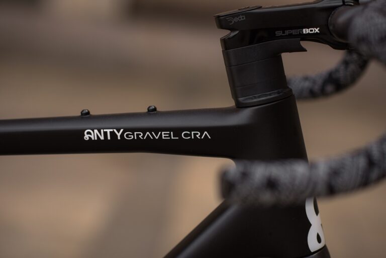 Zbliżenie na matową czarną ramę roweru szutrowego z etykietą „antygravel cra” i kierownicę, w centrum uwagi na pierwszym planie.