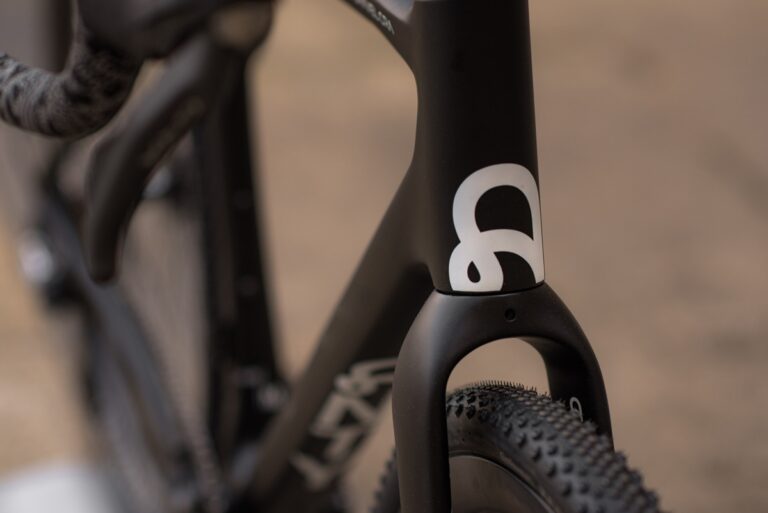 Zbliżenie na czarną ramę roweru z białym logo nr 8, przedstawiające szczegóły bieżnika koła i opony.