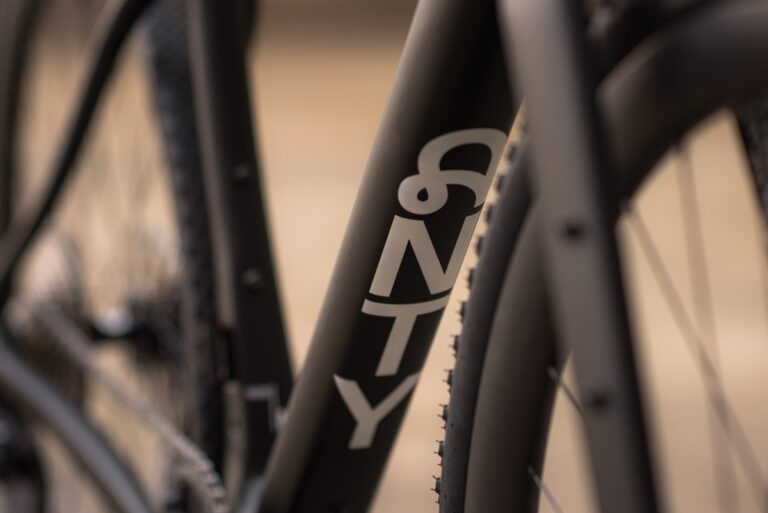 Zbliżenie ramy roweru z logo „6ku” i oponą w nieostrości, podkreślające teksturę i strukturę.