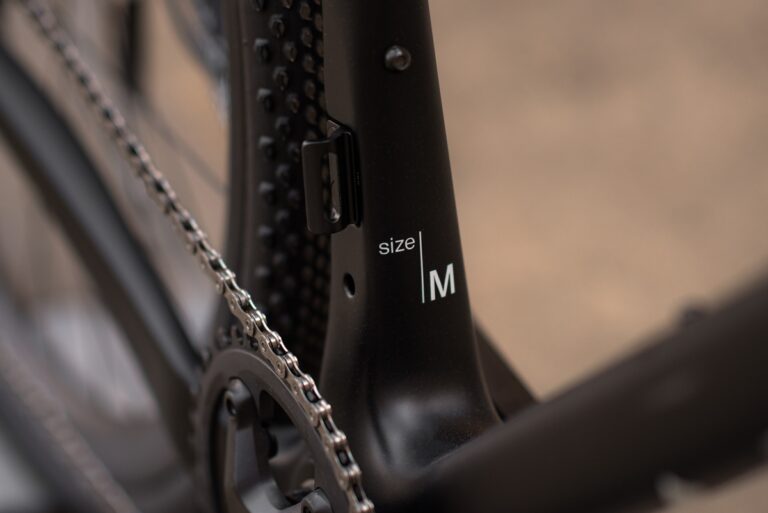 Zbliżenie na czarną ramę roweru z metką z rozmiarem „m” obok łańcucha.
