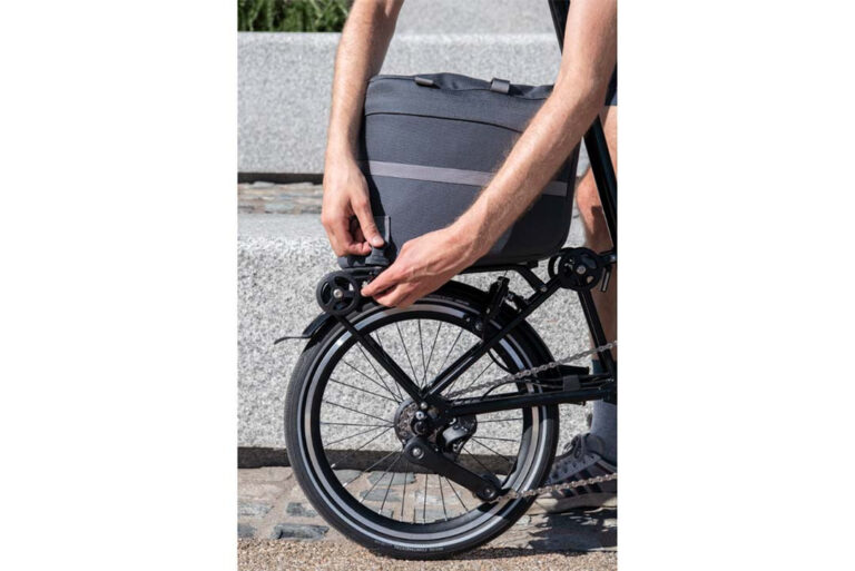 Osoba wkłada na rower torbę na kółkach Torba Brompton Borough Roller Bag - ciemnoszara.